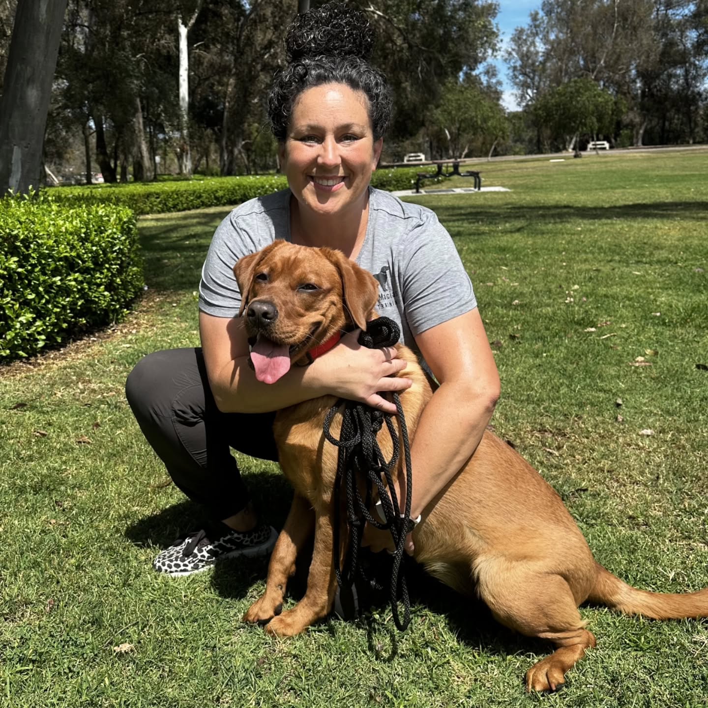 Alexandra Macias crouching in Huntington Central Park with Penny, a brown dog with a red collar, holding a long leash